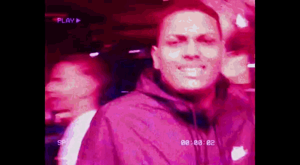 a man in a purple jacket is smiling in a video that is being played