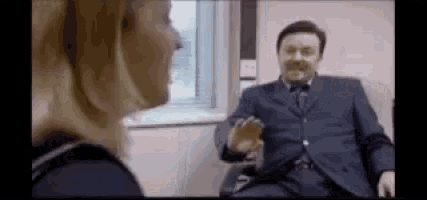 a man in a suit and tie is talking to a woman in a room .