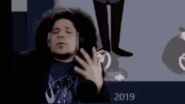 a man wearing headphones stands in front of a wall with the year 2019
