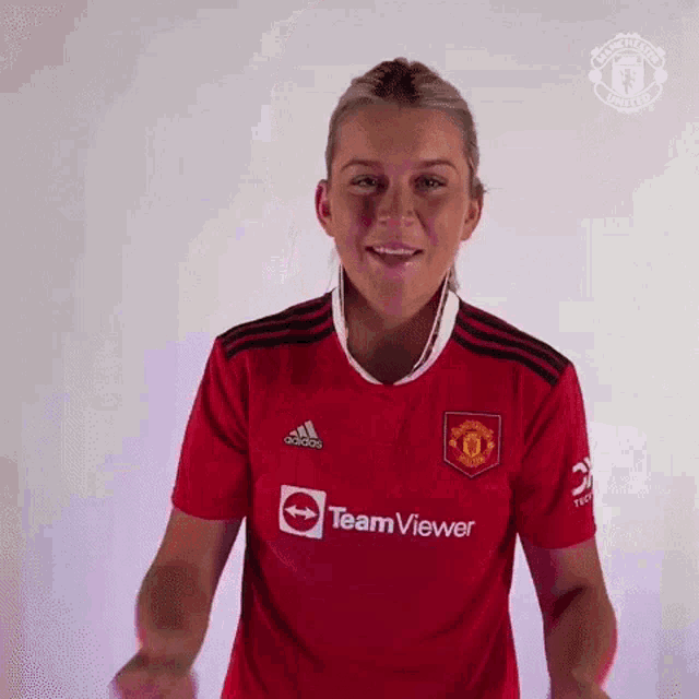 a woman in a red manchester united jersey is smiling and giving a thumbs up .