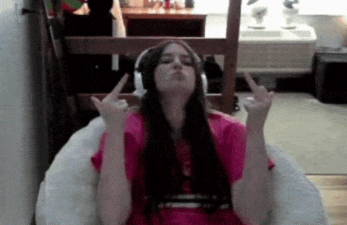 a girl wearing headphones and a pink shirt is giving the middle finger