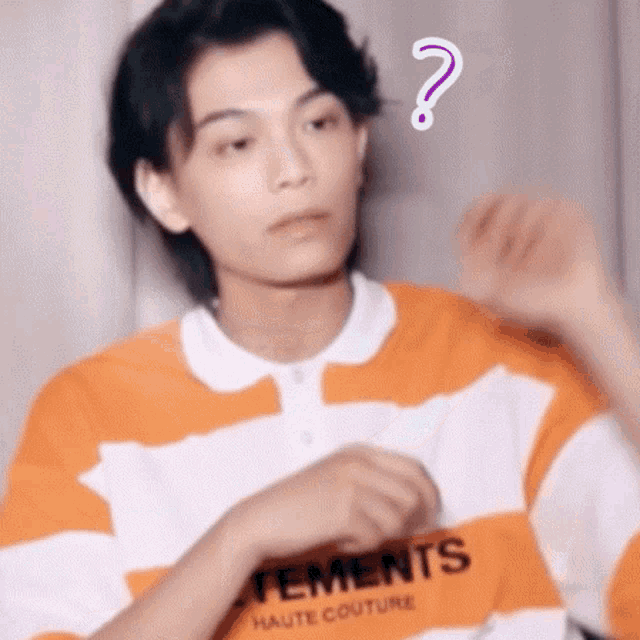 a young man in an orange and white striped shirt is making a funny face with a question mark above his head .