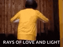 a person in a yellow shirt is dancing in front of a wooden wall with the words `` rays of love and light '' .