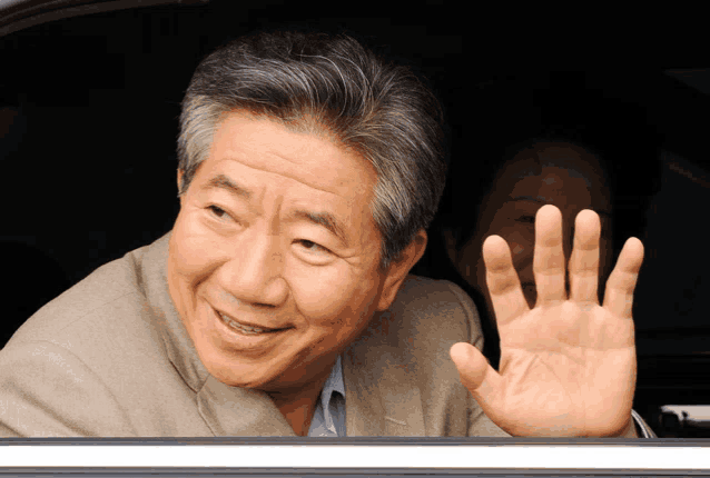 a man in a suit is smiling and waving his hand