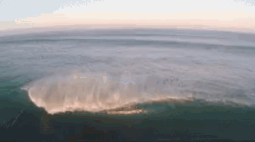 an aerial view of a wave in the ocean with a sunset in the background