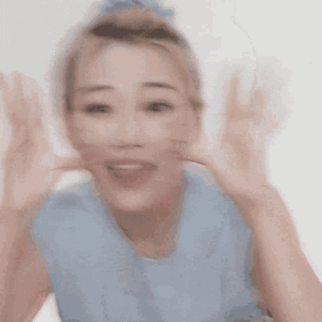 a woman wearing a blue shirt with a butterfly necklace is making a cat face with her hands