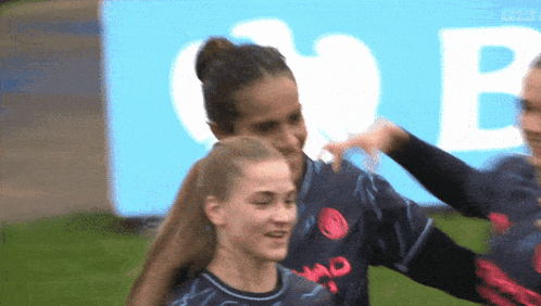 two female soccer players are hugging each other in front of a large b