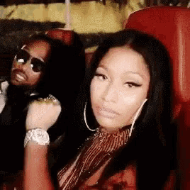 a woman is sitting in a red chair next to a man wearing sunglasses and a watch .