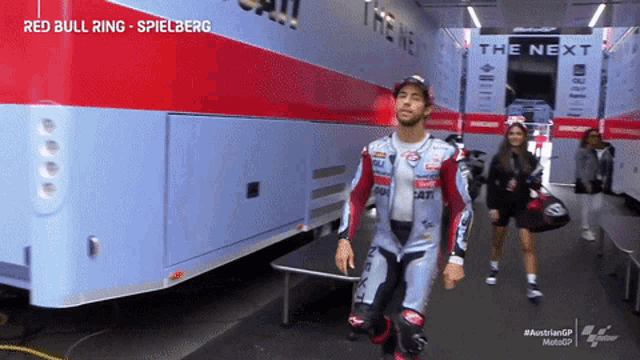 a man in a red bull racing outfit walks in front of a trailer
