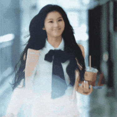a woman wearing a bow tie is walking down a hallway holding a cup of coffee .