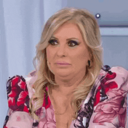 a woman in a pink floral dress is making a funny face while sitting on a chair .