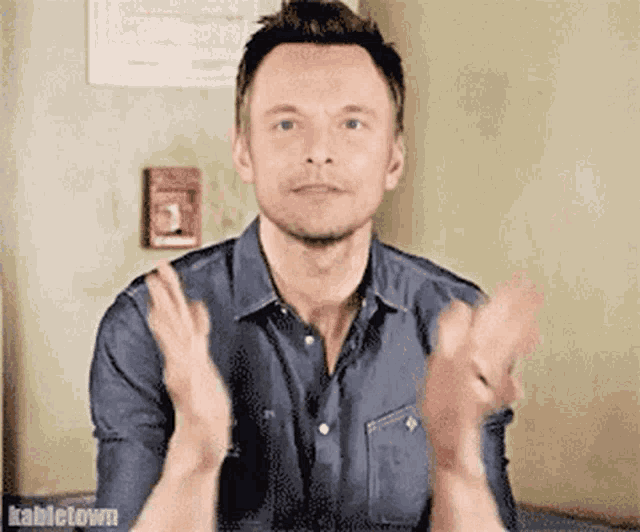 a man in a blue shirt is clapping his hands in front of a fire alarm box