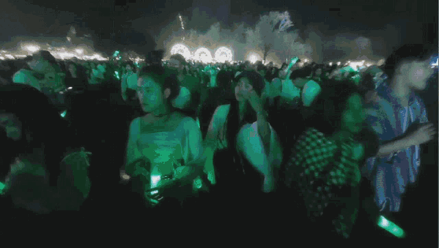 a crowd of people are dancing in a dark room with green lights