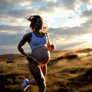 a pregnant woman in a white tank top and shorts is running in a field