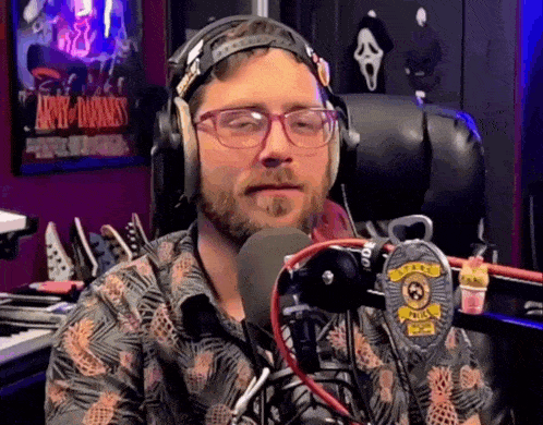 a man wearing glasses and headphones stands in front of a microphone with a badge that says police