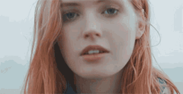 a woman with red hair and blue eyes is looking at the camera .