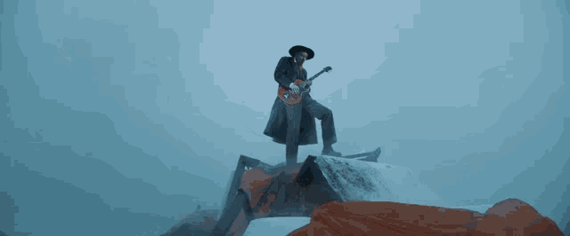 a man in a hat is playing a guitar on top of a rock