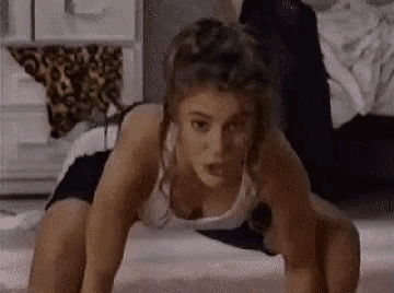 a woman in a white tank top is doing push ups on the floor in a bedroom .