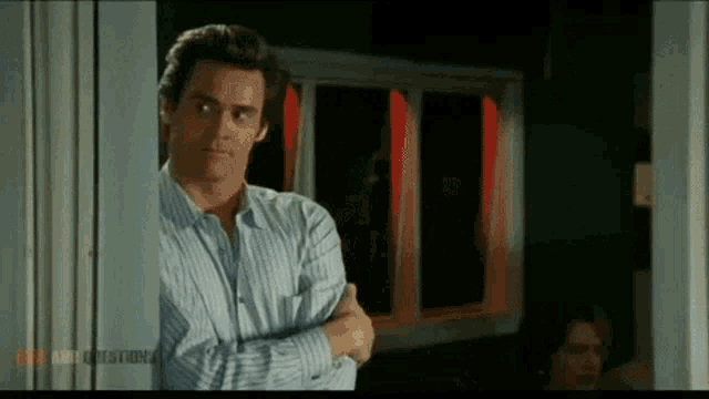 a man in a striped shirt is standing in a doorway with his arms crossed in front of a window .