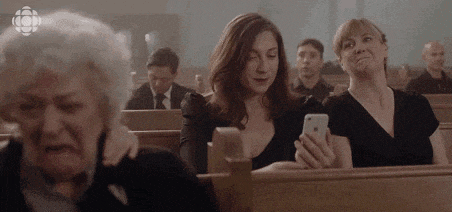 a group of women are sitting in a church and one of them is using a cell phone .