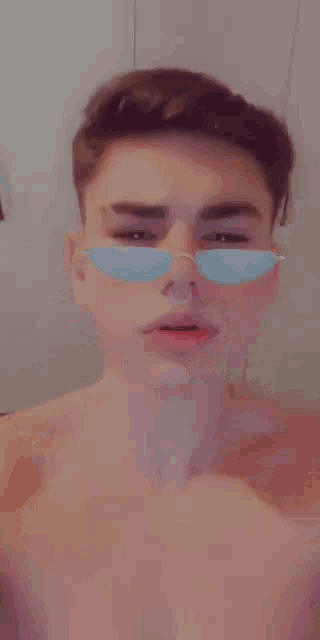 a shirtless young man wearing sunglasses and a nose ring is taking a selfie .