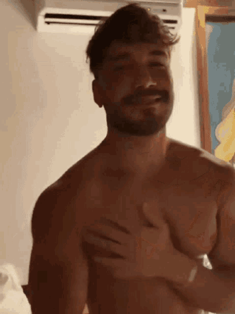 a shirtless man with a beard is smiling and holding his chest .