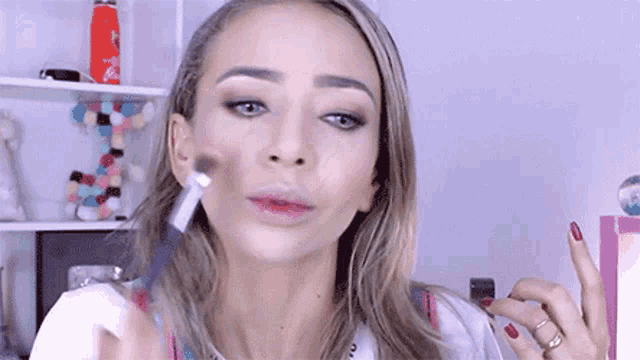 a woman is applying makeup with a brush on her face