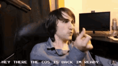 a man is sitting in front of a computer with the words hey there the cos is back im ready below him