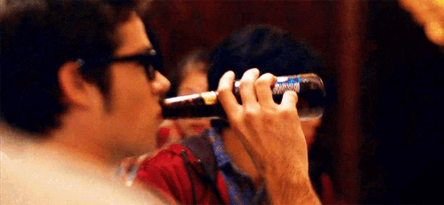 a man is drinking from a pepsi bottle while another man looks on .