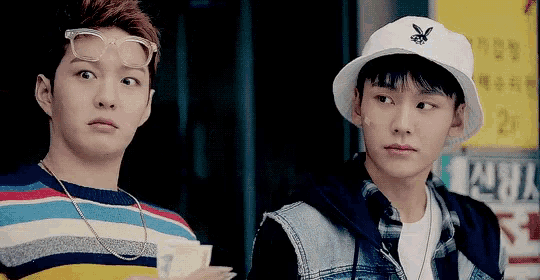 two young men wearing hats and glasses are standing next to each other and looking at each other .