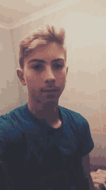 a young man in a blue t-shirt is taking a selfie in a bathroom .