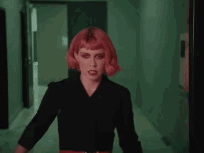 a woman with red hair and black makeup is looking at the camera with a serious look on her face .