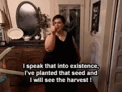 a woman in a black dress is talking on a cell phone while standing in a room .