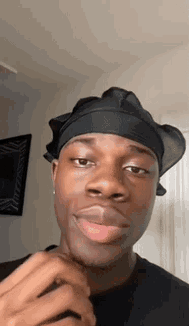 a young man is wearing a black hat and making a funny face .