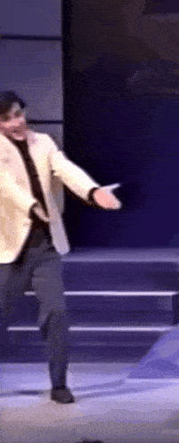 a man in a suit is dancing on a stage with his arms outstretched .