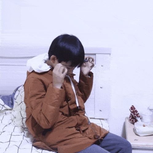 a man in a brown jacket is sitting on a bed with chinese writing behind him