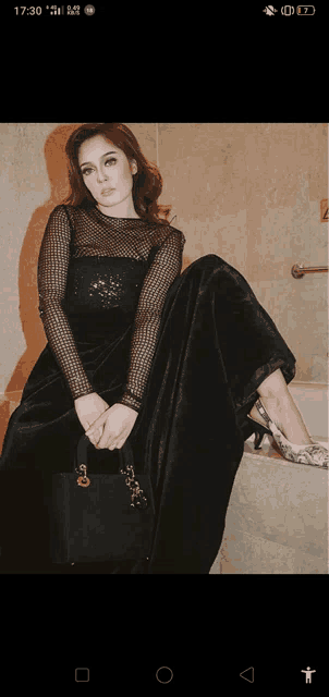a woman in a black dress sits on a bathtub with her legs crossed