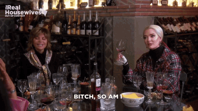 a woman sitting at a table holding a glass of wine says bitch so am i