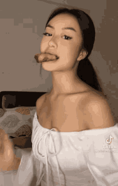 a woman in a white off the shoulder dress is eating a piece of meat .