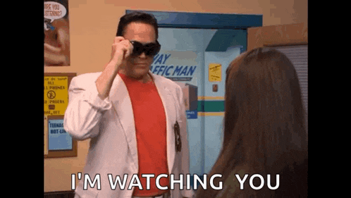 a man wearing sunglasses is standing in front of a woman and says `` i 'm watching you '' .
