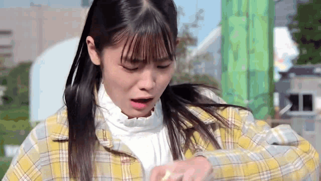 a young girl in a plaid jacket is holding something in her hand and making a face .