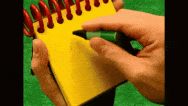 a person holding a yellow notebook with a green marker