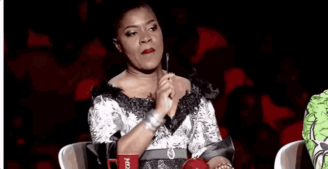 a woman in a black and white dress is sitting in a chair holding a red cup .