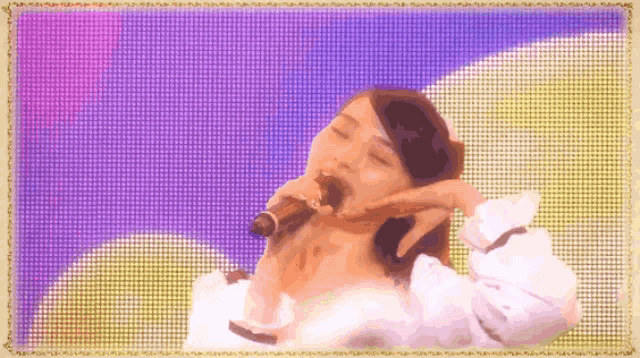 a woman singing into a microphone in front of a purple and yellow background