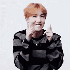 a young man in a striped sweater is giving a thumbs up .