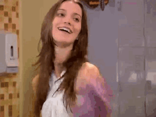 a woman with long hair is standing in a bathroom smiling and waving .