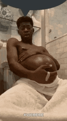 a man is sitting in a bathroom with a towel around his waist and holding his belly .