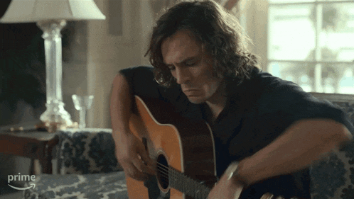a man is playing an acoustic guitar in front of a lamp and the word prime is visible