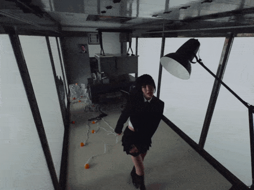 a woman in a black suit is standing in a room with a lamp on the floor
