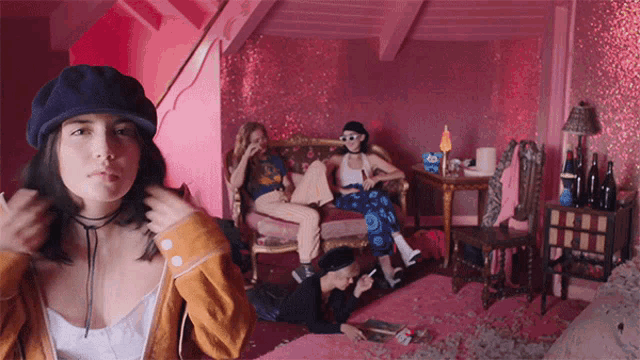 a girl in a blue hat stands in a pink room with other girls